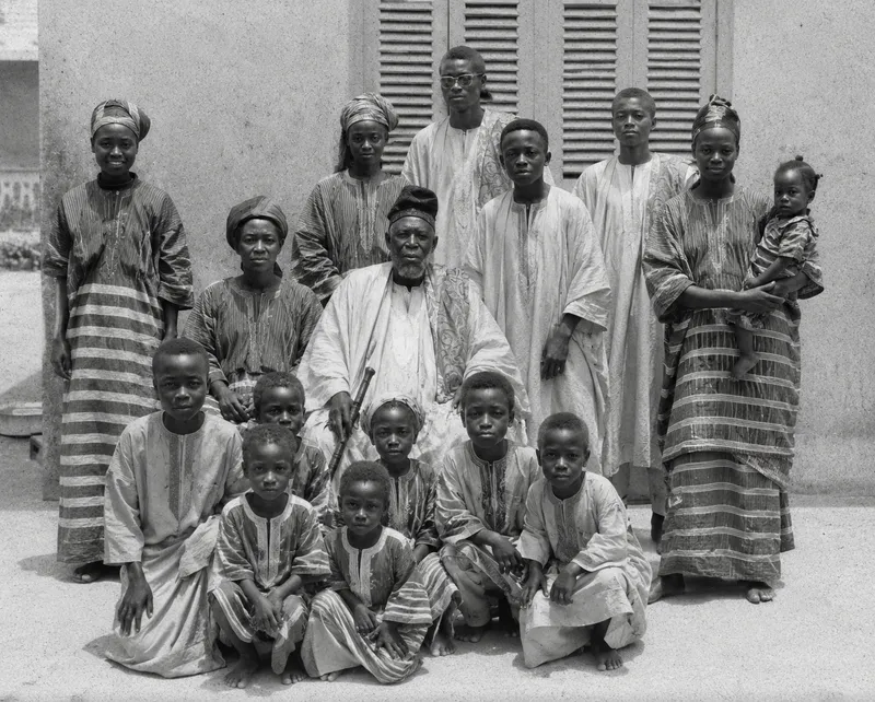 Photo ancienne en noir et blanc d'une grande famille africaine en boubous rayés, autour du patriarche